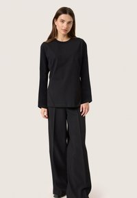 Maglietta nera a maniche lunghe con scollatura a girocollo, abbinata a pantaloni neri a gamba larga. Entrambi i capi hanno una texture liscia e un design minimalista.