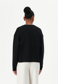 Schwarzes, oversized Sweatshirt aus weichem Stoff, mit Rundhalsausschnitt und überschnittenen Schultern, kombiniert mit hellen Hosen.