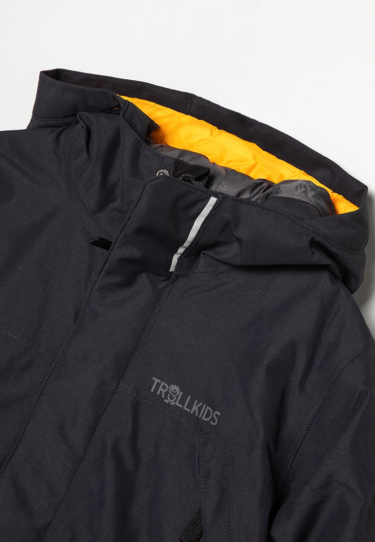 Wasserabweisende schwarze Jacke mit einem gelben Innenfutter. Zu den Merkmalen gehören eine Kapuze, ein vorderer Reißverschluss und Seitentaschen. Das Logo ist auf der Vorderseite sichtbar.