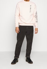 Sudadera rosa claro con texto gr�áfico negro y diseño de dragón en la manga, combinada con pantalones de pana gris oscuro y zapatos negros.