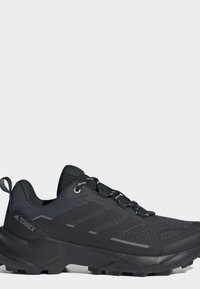 Scarpa da trekking Adidas Terrex nera con suola robusta, tomaia in mesh e chiusura con lacci, vista di lato su uno sfondo chiaro.