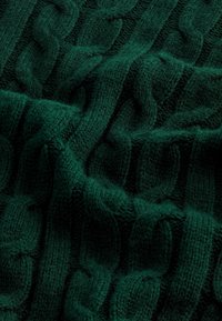 Tissu tricoté vert foncé avec un motif torsadé épais et en relief, et des fibres douces et texturées en vue rapprochée.