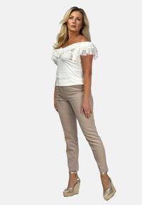 Biała bluzka typu off-the-shoulder z falbanami na rękawach, w połączeniu z beżowymi dopasowanymi spodniami i złotymi koturnami, prezentującymi gładką teksturę.