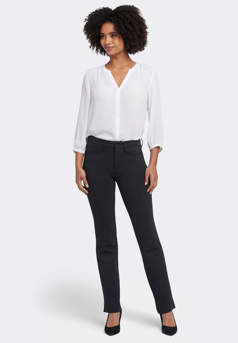 Vit blus med långa ärmar, V-ringning och knapprad, kombinerad med svarta, smala byxor. Modellen bär svarta högklackade skor.