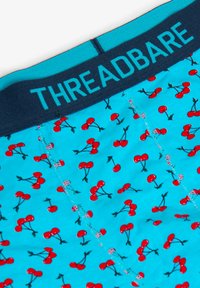 Boxer blu con motivo di ciliegie rosse. La vita è blu scuro con la scritta "THREADBARE" in azzurro. Tessuto morbido ed elastico.