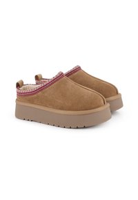 Zapatos slip-on de ante marrón con suela de goma texturizada, que cuentan con un acento tejido en rojo y blanco a lo largo del borde superior y una pestaña trasera para tirar.
