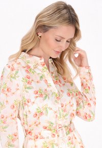 Blomstret skjortekjole i let stof, med et pastelfarvet roseprint, knaplukning foran, lange ærmer og en bælte i taljen for at fremhæve formen.