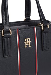 Τσάντα ώμου σε ναυτικό μπλε με υφή, διπλές λαβές, κάθετες κόκκινες και λευκές ρίγες, και χρυσόλογο Tommy Hilfiger στην μπροστινή πλευρά.