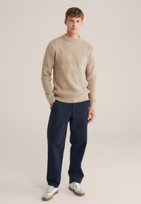 Beige kötött pulóver textúrált mintával, kerek nyakkal, navy kék chino nadrággal és fehér sportcipővel, világosszürke részletekkel párosítva.