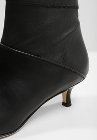 Botte en cuir noir avec une cheville ajustée, un petit talon et une texture lisse. Présente une couture latérale et des accents matériels minimaux.