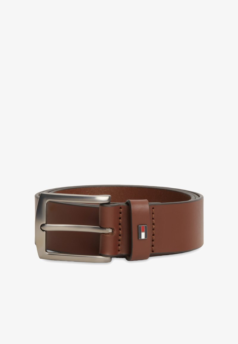 Ceinture en cuir marron avec boucle en métal argenté et petit emblème rectangulaire aux couleurs rouge, blanc et noir sur la boucle de ceinture.