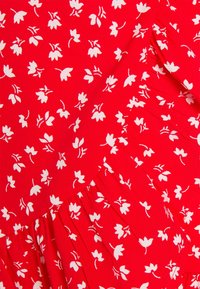 Tejido rojo con un patrón floral blanco que presenta pequeñas hojas y flores, con un detalle plisado en el dobladillo. Textura ligera.