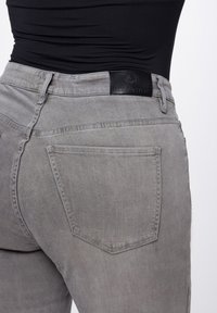 Grijze jeans met een slim fit, met een gestructureerde afwerking, contrasterende stiksels en een zwart leren label bij de tailleband. Twee achterzakken zichtbaar.