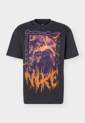 Black T-shirt featuring a large graphic of a goat with curved horns framed by purple chains and orange flame-style text reading "NIKE."