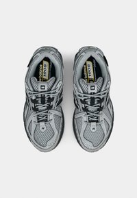 Harmaat urheilukengät, joissa on verkkomateriaalia ja synteettisiä kerroksia. Varustettu mustilla nauhoilla ja yksityiskohdilla, pehmustetulla nilkkaosalla ja kuvioidulla kumipohjalla.