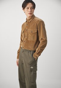 Brun kordfløyelskjorte med knappestandard, to brystlommer, kragedesign. Kombinert med lyse olivengrønne cargos med en lappelomme.