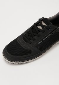 Pantofii sport negri, fabricați din plasă și piele, cu șireturi rotunde, cusături contrastante și o talpă din cauciuc, având un logo pe lateral.