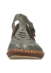 Zapato de cuero verde con diseño trenzado, correa ajustable y costuras en tono marrón contrastante a lo largo de la suela. Suela plana con patrón de tracción.