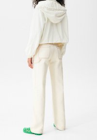 Jasna, krótka kurtka z kapturem, zestawiona z kremowymi szerokimi spodniami i zielonym obuwiem z wycięciami.