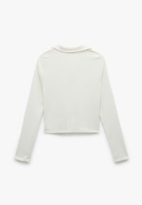 Witte cropped longsleeve shirt van een zachte, gestructureerde stof. Voorzien van een klassieke kraag en een licht rafelige zoom bij de mouwen en onderkant.