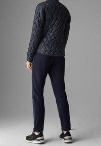 Tmavě modrá prošívaná péřová bunda s přiléhavým střihem, doplněná tmavě modrými tepláky. Černé sportovní boty se zelenými detaily dokončují outfit.