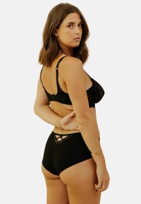 Soutien-gorge noir avec bordure en dentelle, doté de bretelles ajustables et d'une fermeture à crochets, associé à des culottes taille haute assorties présentant un design découpé géométrique.