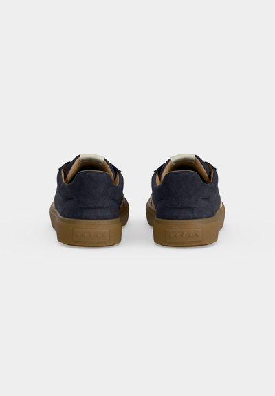 Paire de baskets en daim bleu marine avec semelles en caoutchouc marron clair, vues de dos sur fond blanc.