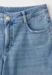 Lichtblauwe denim jeans met tailleband, voorknop, lussen voor een riem en een voorzak zichtbaar tegen een witte achtergrond.