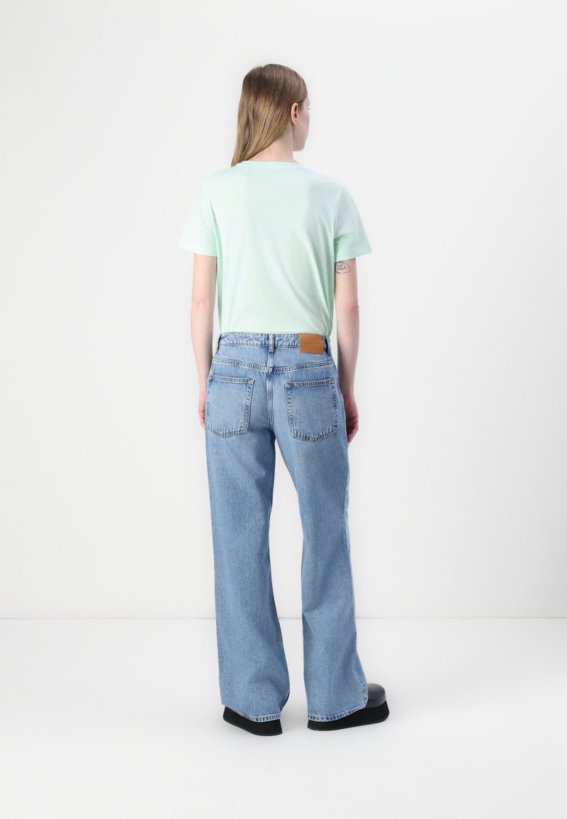 Licht muntgroene katoenen T-shirt gecombineerd met high-waisted lichtblauwe spijkerbroek. De spijkerbroek heeft een bruine leren patch en een wijd model.