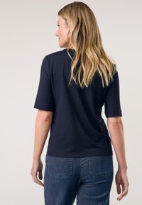 Navyblaues Kurzarm-T-Shirt mit Rundhalsausschnitt und glatter Textur, kombiniert mit dunklen Jeanshosen mit Rückentaschendetails.