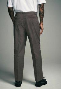 Brown pinstriped trousers with a tailored fit, featuring two back pockets and a flat front, paired with black chunky shoes.