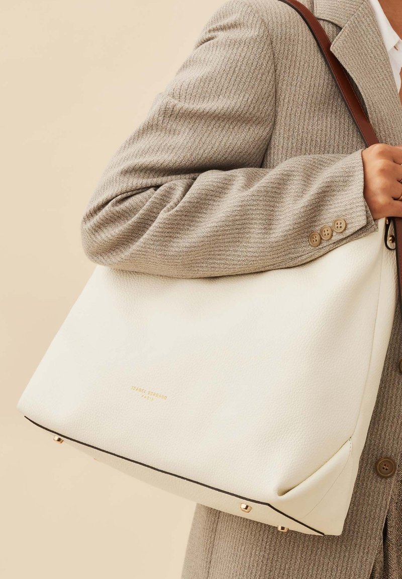 Large white leather tote bag with a textured surface, brown leather shoulder strap, and gold hardware accents. Features a minimalist design.
