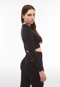 Crop top aderente nero a maniche lunghe abbinato a leggings high-waisted con una texture a costine. Presenta un design cropped e un semplice dettaglio con logo.