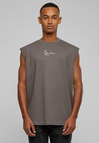 Grå ärmlös t-shirt med rund halsringning, tillverkad av mjukt material, med en vit signaturlogotyp på bröstet. Enkelt design, avslappnad passform.