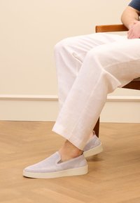 Grijze instapschoenen met een bovenkant van mesh en een lichte zool, voorzien van uitsnijdingen en een gevoerde kraag voor comfort, gecombineerd met witte linnen broeken.