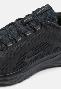 Black athletic shoe featuring mesh and textile upper, padded tongue, reflective accents, and a textured sole with Nike logo.