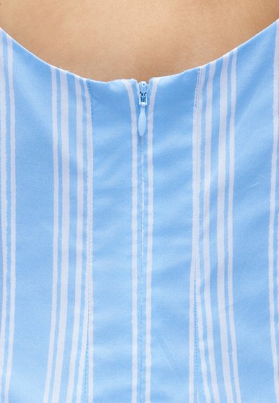 Κοντινό πλάνο ενός κάθετου φερμουάρ σε ένα ρουχισμό με γαλάζιες και λευκές ρίγες πάνω σε γυμνό δέρμα.