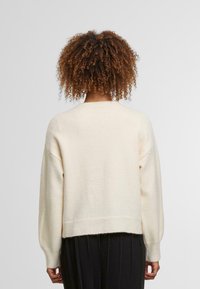 Krémová, měkká pletená svetr s žebrovanými manžetami a spodním lemem, s uvolněným střihem a spuštěnými rameny. Zadní pohled, bez vzorů nebo akcentů.