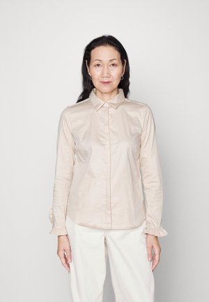 Lys beige langermet skjorte med krage, volangmansjetter og knapp-fram design, laget av glatt stoff og tilpasset fasong.