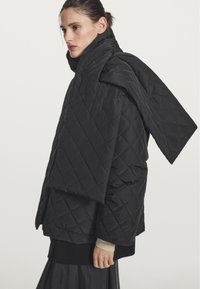 Black quilted puffer jacket with an oversized collar and long, draped sleeves. Features a smooth texture and a loose fit.