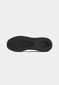 Black rubber sneaker sole with textured surface and deep treads for traction. Curved heel and raised brand logo visible.