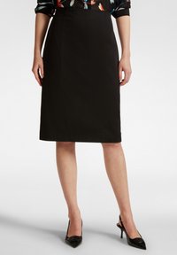 Gonna nera a matita realizzata in un tessuto liscio, lunghezza al ginocchio e con una silhouette aderente. Abbinata a tacchi a punta neri per un look elegante.