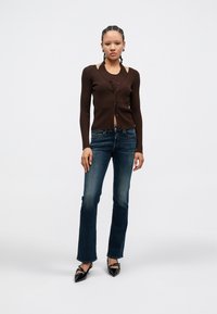 Καφέ ριγωτή ζακέτα με κούμπωμα με κουμπιά, σε συνδυασμό με τζιν καμπάνα σκούρου μπλε και μαύρες γόβες με μυτερή μύτη. Απλός σχεδιασμός, εφαρμοστή σιλουέτα.