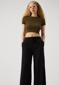 Camiseta corta de rayas verdes combinada con pantalones de pierna ancha negros, con cinturilla elástica y bolsillos laterales. Gafas de sol rectangulares transparentes de color rosa.