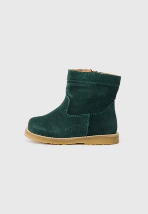 Stivaletto in camoscio verde con punta rotonda, suola piatta beige e canna corta; presenta cuciture tono su tono e chiusura con zip sul lato.