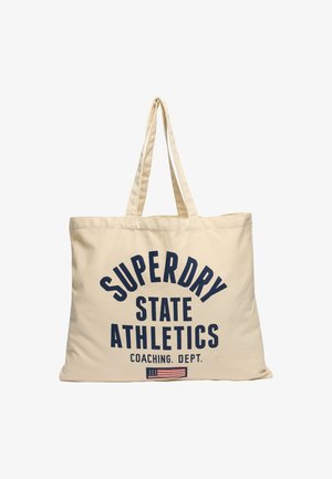 Bolsa de tela beige con dos asas. En la parte frontal presenta un texto en azul marino: "SUPERDRY STATE ATHLETICS COACHING DEPT." y una pequeña gráfica de la bandera americana.