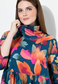 Šaty s květinovým potiskem na tyrkysovém pozadí s výraznými oranžovými a růžovými květy, vysokým límcem, dlouhými rukávy a stupňovaným lemem.