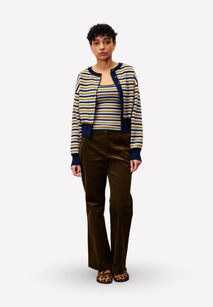 Cardigan rayé en marine, moutarde et blanc, porté sur un débardeur assorti ; associé à un pantalon en velours côtelé marron foncé à jambes larges et à des chaussures à imprimé léopard.