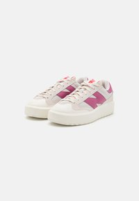 Zapatillas con parte superior beige, acentos rosas, materiales de malla y ante, cordones texturizados y una suela gruesa de goma blanca.