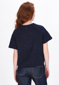 Navyblauw breisel met korte mouwen, met een gestructureerd ribpatroon en subtiele vlekken. Het achteraanzicht toont een ontspannen pasvorm en een ronde hals.